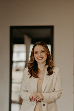 a woman standing in front of a door wearing a white jacket and tan dress shirt