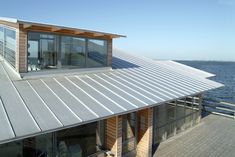 a house on the water with a metal roof and large windows that overlooks the ocean