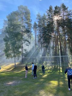 several people are standing in the grass near trees and a volleyball net on a sunny day