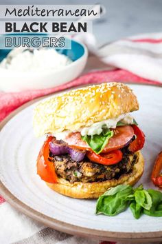 a burger with tomatoes, onions and lettuce on a white plate