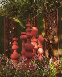 an array of vases and flowers in front of a green wall with intricate carvings