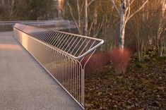 a metal fence on the side of a road next to some trees and bushes at sunset