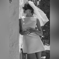 black and white photograph of a woman in sunglasses leaning against a wall wearing a wedding dress