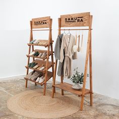 two wooden racks with clothes hanging on them in front of a white wall and round rug