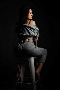 a woman is sitting on a stool with her back to the camera and looking off into the distance