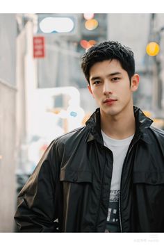 a young man standing in the middle of an urban street wearing a black jacket and white t - shirt