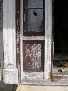 an old door with peeling paint and broken glass on the front porch, next to a pile of junk