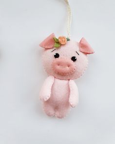 a pink pig ornament hanging from a string on a white background with flowers