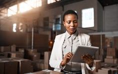 a woman in a warehouse looking at something on her tablet computer while she is surrounded by boxes