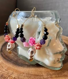 a pair of earrings with flowers and skulls hanging from them on a wooden table next to a candle