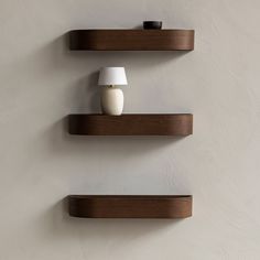 two wooden shelves on the wall with a white vase and lamp next to them,