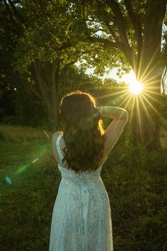 a woman in a white dress is looking at the sun