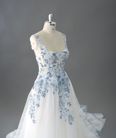 a white and blue wedding dress with flowers on the bouncy skirt is displayed in front of a mannequin