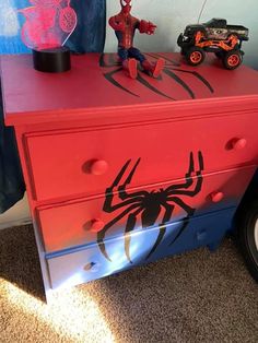 a red and blue dresser with a spiderman painted on the top, next to a toy car