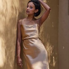 a woman leaning against a wall with her hand on her head wearing a gold dress