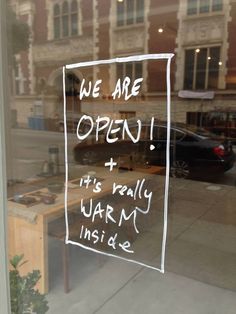 an open sign on the glass door of a store front window that says, we are open it's really warm inside