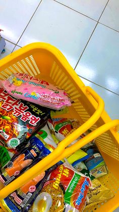 a yellow shopping basket filled with candy and snacks on top of a white tiled floor