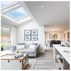 a living room filled with furniture next to a window covered in skylights and framed pictures