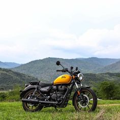 a yellow and black motorcycle parked on top of a lush green field with mountains in the background