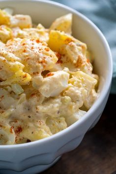 a white bowl filled with macaroni salad on top of a wooden table next to a blue towel