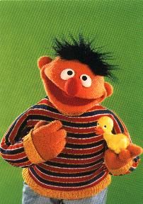 the sesame character is holding a rubber duck in his right hand and wearing a striped sweater