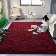 a woman sitting on the floor reading a book in front of a red area rug