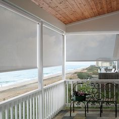 a balcony with a bench and some blinds on the windows overlooking the beach in front of it