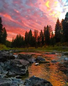 the sun sets over a river with rocks and trees