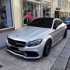 a silver car parked in front of a building on the side of a street next to other cars