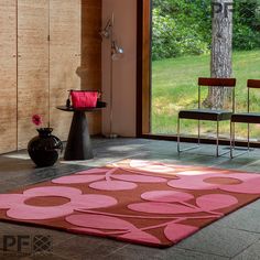 a living room with a pink rug and two chairs in front of a large window