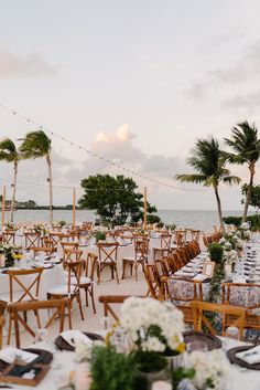 tables and chairs are set up on the beach for an outdoor wedding reception with palm trees in the background