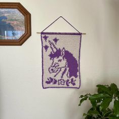 a crocheted unicorn is hanging on the wall next to a potted plant