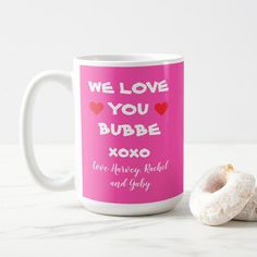 a pink coffee mug next to two donuts on a white table with the words, we love you bubbae xoxo