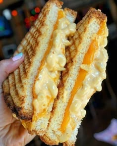 a hand holding a grilled cheese sandwich in front of the camera with macaroni and cheese on it