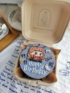 a birthday cake in an open box with writing on the table next to other items