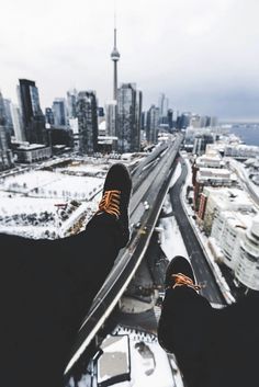 someone standing on top of a building with their feet in the air looking down at a city