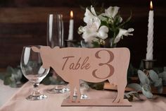 a wooden table number sitting on top of a table next to wine glasses and flowers