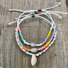 the multi - colored beaded bracelets are arranged on a wooden surface with shells and beads