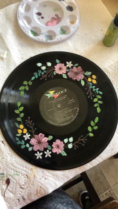 a black plate with flowers painted on it next to a white bowl and saucer