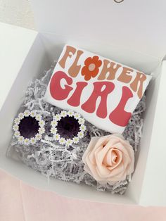 a flower girl cake in a box with sunglasses and flowers on the side, next to a pink rose