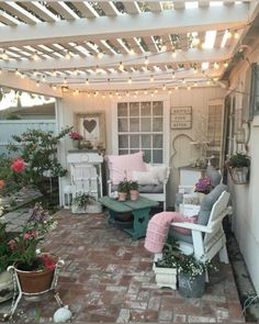 a patio covered in lots of potted plants next to a white house with lights on the roof