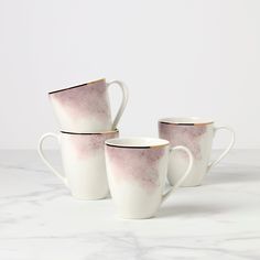 three white and pink coffee mugs sitting on top of a marble countertop next to each other