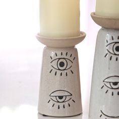 two ceramic candlesticks with eyes painted on them, one has a candle in the middle