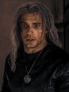 a man with long hair wearing a black shirt and chain around his neck is staring at the camera