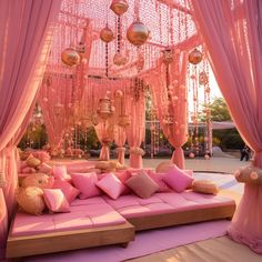 a bed covered in lots of pink pillows under a canopy with hanging lights on it