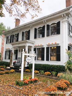 a large white house with black shutters on the front and side windows in autumn