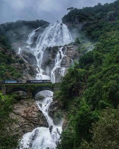 a train traveling over a bridge in front of a waterfall with water pouring from it