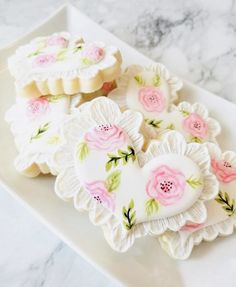 heart shaped cookies decorated with pink flowers on a white plate next to marble counter top