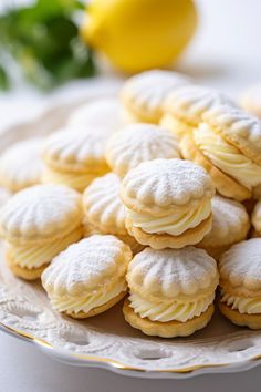 a white plate topped with cookies covered in powdered sugar next to lemon wedges