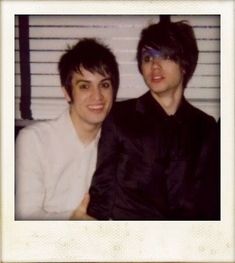 two young men sitting next to each other in front of a white shuttered wall